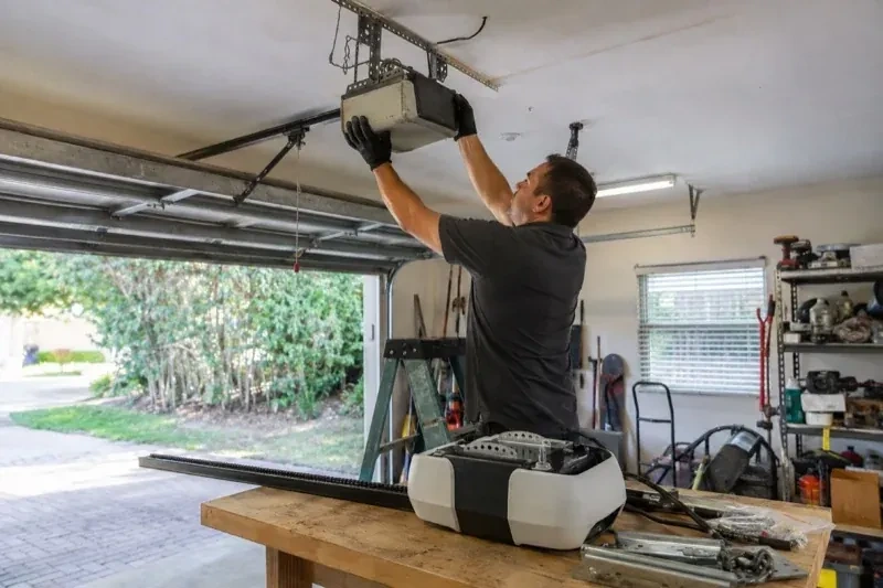 Person holding an overhead garage-door opener beside another opener and hardware on a workbench — Garage Door Opener Replacement, Doon