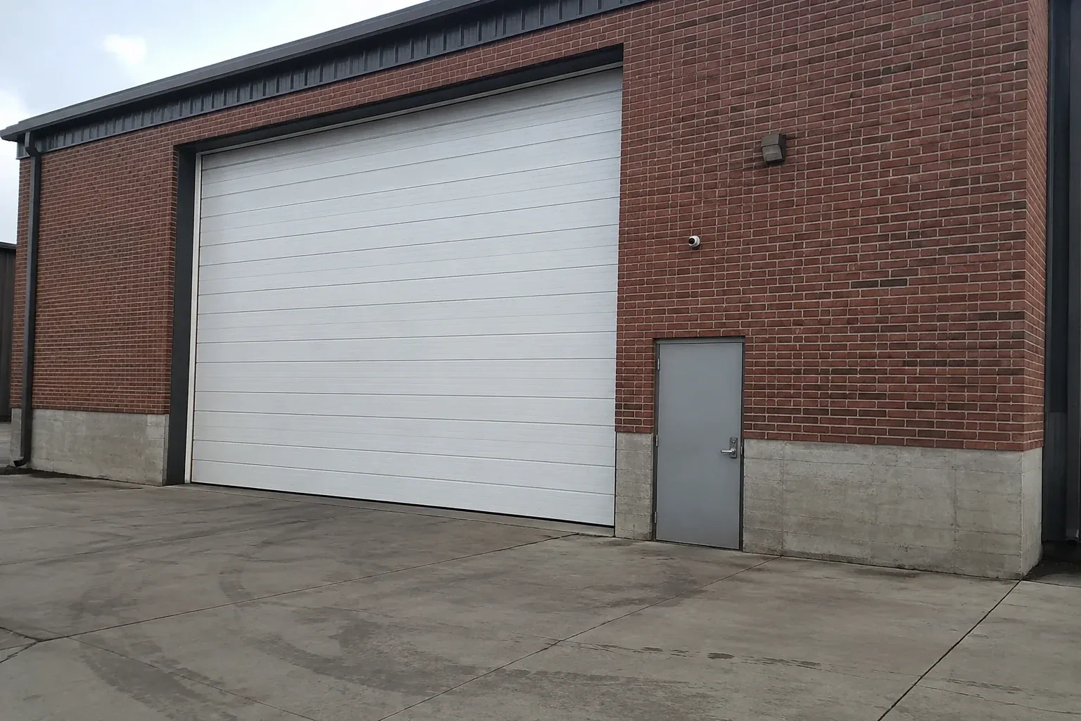 Tall closed sectional loading door beside a personnel door at a brick unit. — Commercial Sectional Door Repair, Kitchener